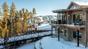 A modern two-story building with a balcony overlooking a snowy landscape and a ski slope. - 9 Deep Forest Drive 6 Bedroom Home by Moonlight Basin Lodging (Big Sky)