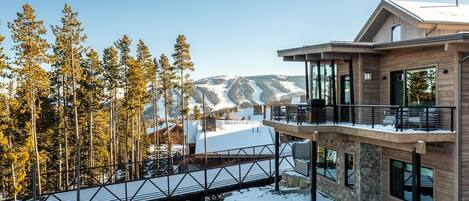 A modern two-story building with a balcony overlooking a snowy landscape and a ski slope.