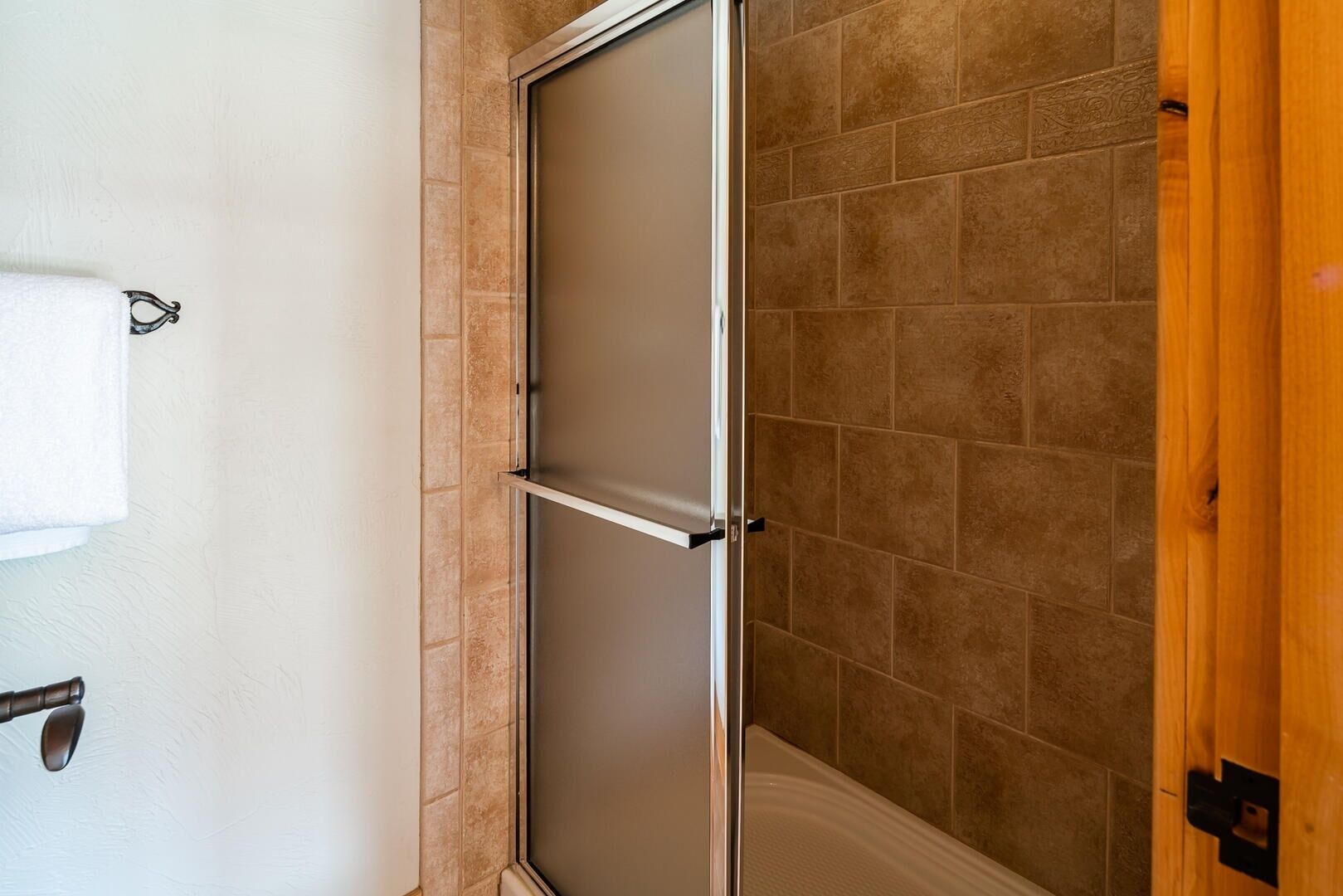 A bathroom with a shower enclosure, a towel rack, and a wooden door.