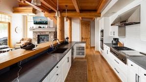 Une cuisine moderne dotée d’une cheminée en pierre, de poutres en bois et d’un grand îlot central avec un évier.