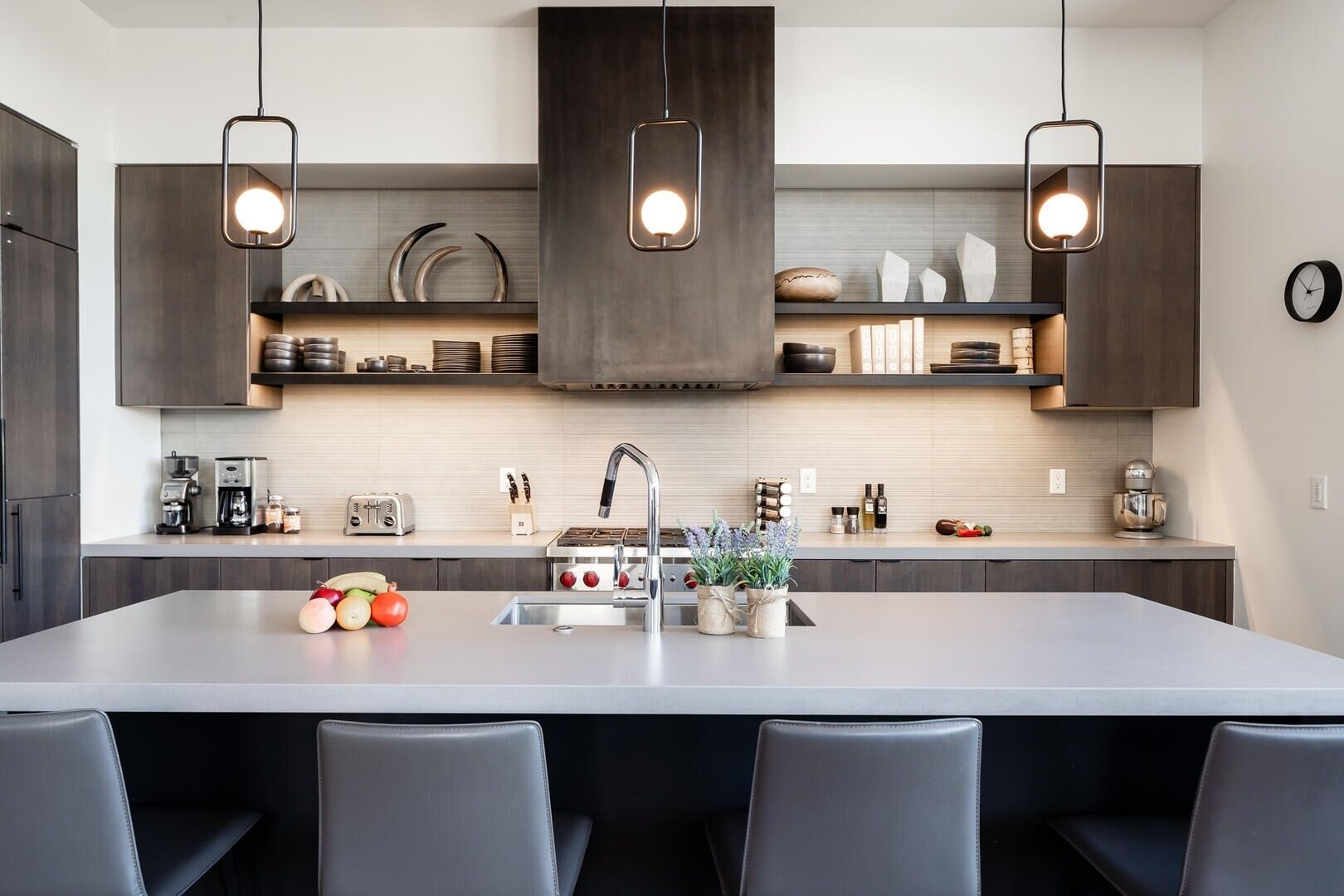 Une cuisine moderne dotée d’un îlot central, d’appareils électroménagers en acier inoxydable et de luminaires suspendus.