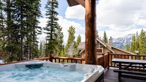 A hot tub on a wooden deck with a wooden railing, surrounded by trees and a mountain view. - 6 Mountain Home Road 4 Bedroom Home by Moonlight Basin Lodging (Big Sky)