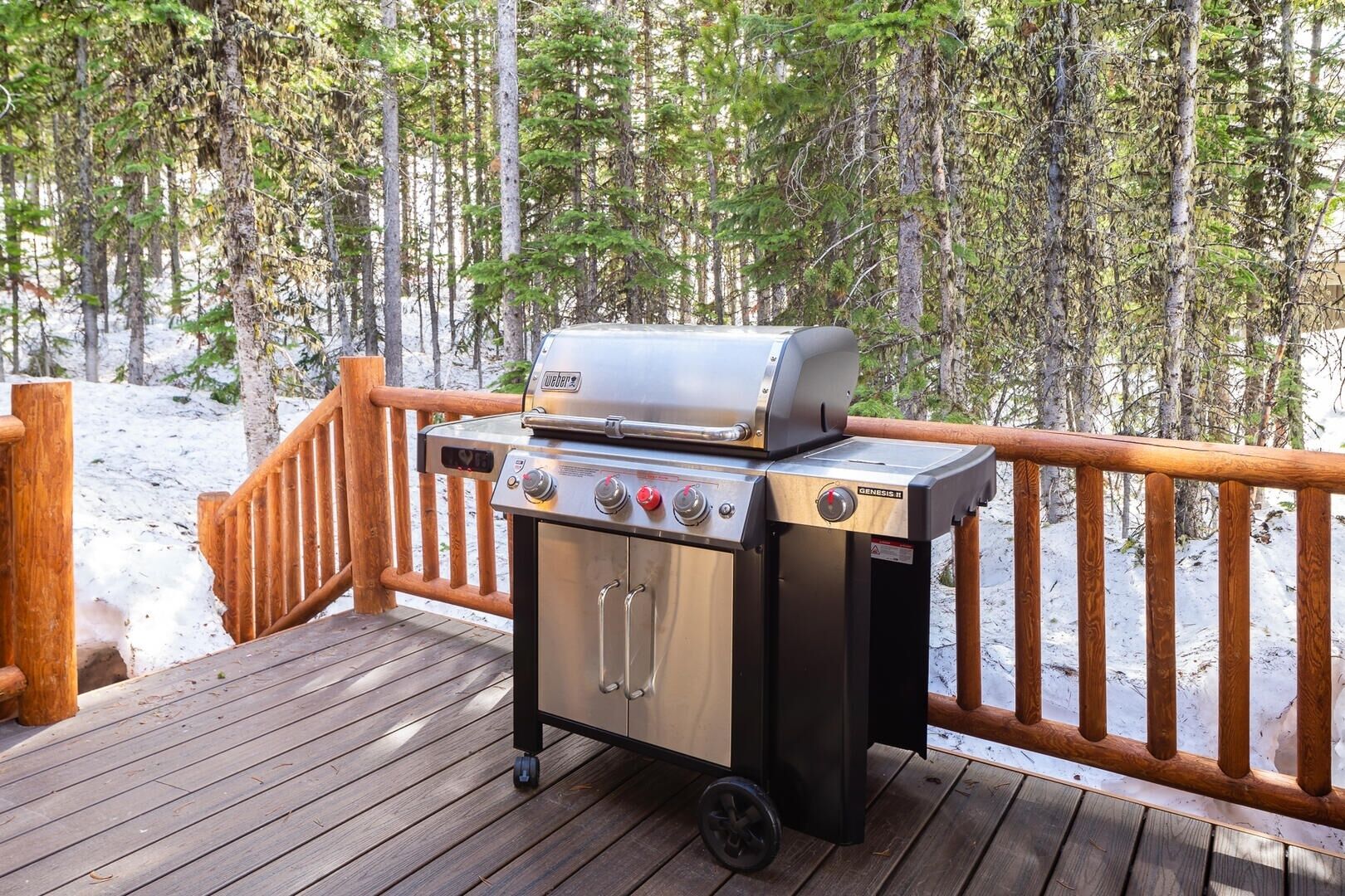 Un barbecue Genesis II portable, placé sur une terrasse en bois dotée d’une rambarde en bois, entouré d’un paysage enneigé et d’arbres.