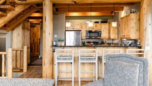A rustic wooden interior with a kitchen area featuring wooden cabinets, a stainless steel refrigerator, and a bar with stools. - 3 Bandit Way 4 Bedroom Home by Moonlight Basin Lodging (Big Sky)