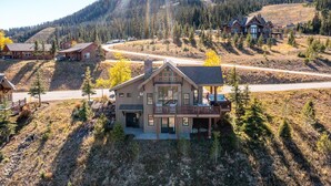 A large log cabin with a balcony, surrounded by a mountainous landscape and other cabins. - 3 Bandit Way 4 Bedroom Home by Moonlight Basin Lodging (Big Sky)