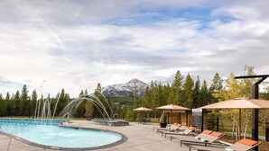 A pool with a water feature, lounge chairs, and a mountain view. - 215 Lakelodge 2 Bedroom Condo by Moonlight Basin Lodging (Big Sky)