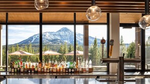 A bar with a mountain view, bottles of alcohol, and a beer tap. - 215 Lakelodge 2 Bedroom Condo by Moonlight Basin Lodging (Big Sky)