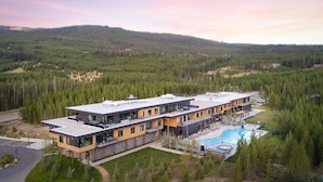 A modern multi-story hotel with a pool, surrounded by dense forest and hills. - 215 Lakelodge 2 Bedroom Condo by Moonlight Basin Lodging (Big Sky)