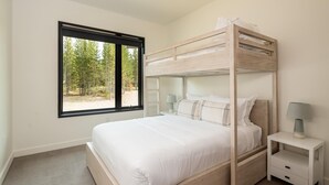 A bunk bed with a view of trees through a window, a bedside table with a lamp, and a nightstand with a drawer. - 221 Lakelodge 2 Bedroom Condo by Moonlight Basin Lodging (Big Sky)