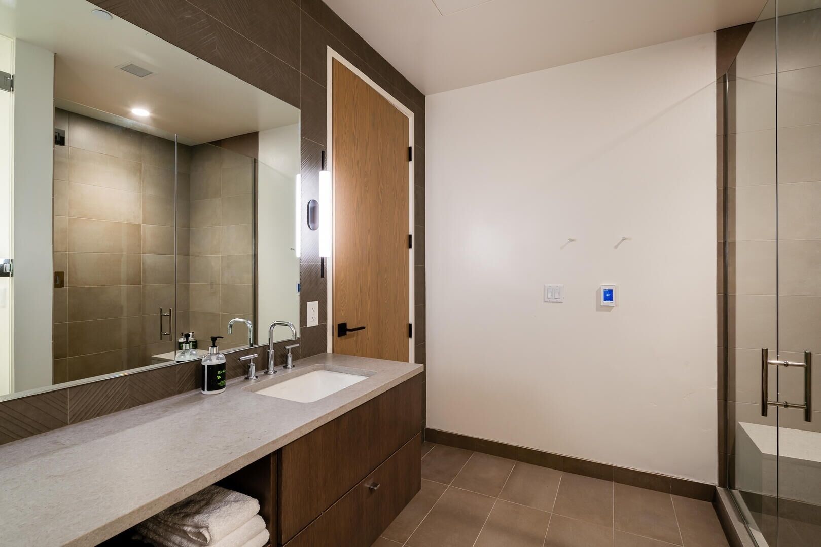 Une salle de bain moderne avec un grand miroir, deux lavabos, une douche et un porte-serviettes.