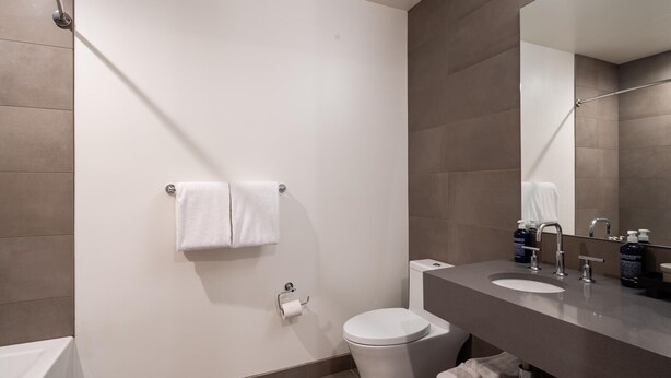 Une salle de bain moderne avec des toilettes, un lavabo et un miroir. On y trouve des serviettes et des articles de toilette sur le comptoir.