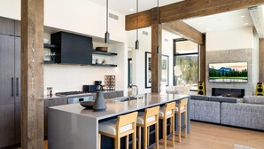 Une cuisine moderne dotée d’un îlot central, de meubles de rangement aux couleurs sombres et d’une grande fenêtre.
