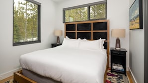 A bedroom with a large bed, two bedside tables, a headboard with a grid pattern, and two windows. - 27 Lake Cabin 3 Bedroom Home by Moonlight Basin Lodging (Big Sky)