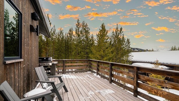 A wooden deck with outdoor seating, overlooking a snowy landscape and trees. - 27 Lake Cabin 3 Bedroom Home by Moonlight Basin Lodging (Big Sky)