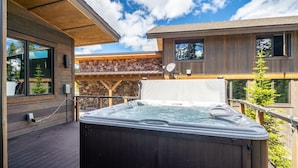 A wooden deck with a hot tub, a bench, and a stone wall. - 8 Alpine Bend 3 Bedroom Home by Moonlight Basin Lodging (Big Sky)