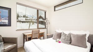 A hotel room with a large bed, a desk, and a chair. There is a window with a view of snow-covered mountains. - 8 Alpine Bend 3 Bedroom Home by Moonlight Basin Lodging (Big Sky)