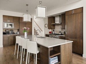 Een moderne keuken met een centraal eiland, barstoelen, een koffieapparaat en een fornuis.