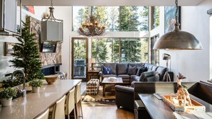 A modern living room with a fireplace, a large window, and a cozy seating area. - 8 Alpine Bend 3 Bedroom Home by Moonlight Basin Lodging (Big Sky)