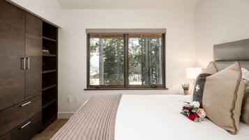 A bedroom with a large window, a bed with pillows, a bedside table with a lamp, and a wardrobe.
