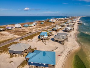 Vista aérea de una zona costera con casas de playa, una carretera y un muelle que se adentra en el agua.