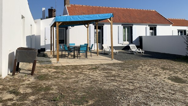 Un espace extérieur abrité avec des tables et des chaises, un bâtiment blanc avec un toit recouvert de tuiles rouges et un ciel bleu dégagé.