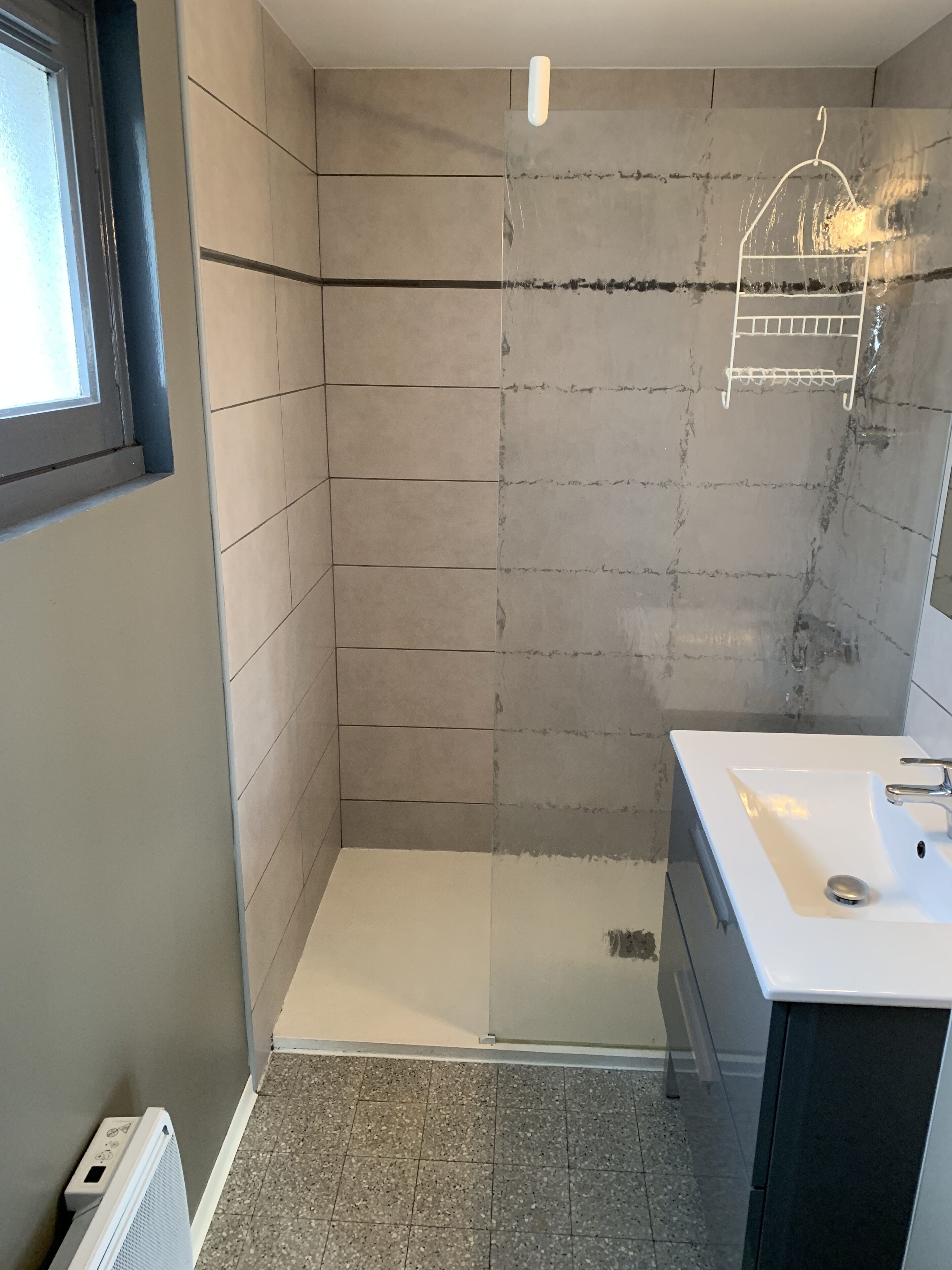 A bathroom with a shower, a sink, and a window.