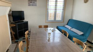 Un coin repas comprenant une table, des chaises, un téléviseur et un canapé bleu.