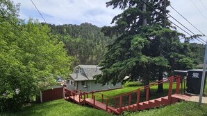 Ein Haus mit einer roten Freitreppe, umgeben von üppiger Vegetation und einem bewaldeten Hügel im Hintergrund.