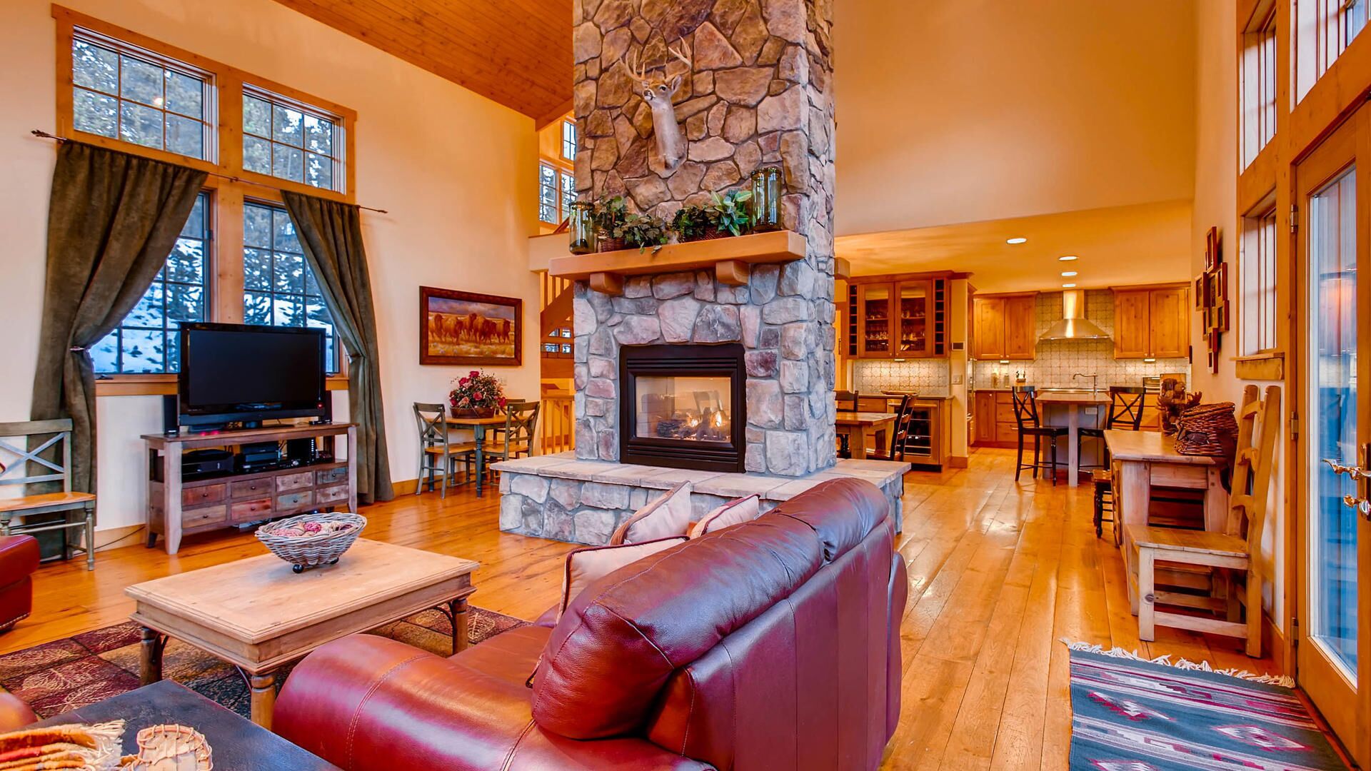 A spacious living room with a stone fireplace, leather sofa, and a television.