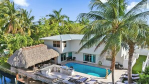 A modern resort with a swimming pool, a bar area, and a thatched-roof structure.