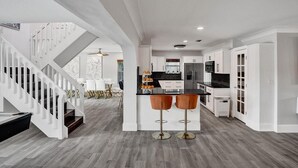 A modern kitchen with white cabinetry, a central island with stools, and a staircase leading to another level.