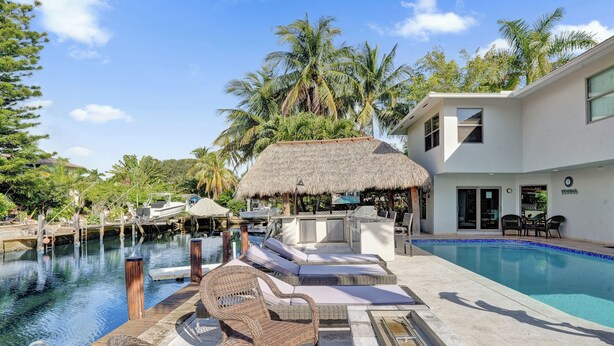 A pool area with lounge chairs, a thatched-roof structure, and a building with a sign.