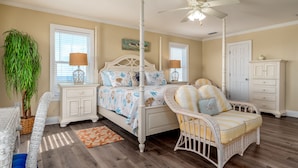 A bedroom with a four-poster bed, a ceiling fan, a large potted plant, wicker furniture, and a wooden floor. - Ocean view, steps from water, private bedroom balcony! - Shore Beats Work (Dauphin Island)