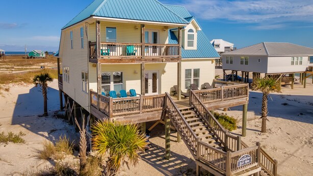 A two-story beach house with a balcony, a deck, and a staircase leading to the upper floor. - Ocean view, steps from water, private bedroom balcony! - Shore Beats Work (Dauphin Island)