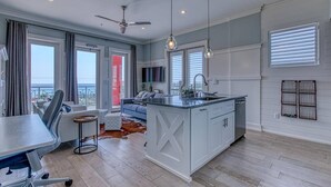 A modern kitchen with a central island, a dining area with a table and chairs, and a living area with a sofa and a TV. - FantaSea On 30A - Gulf View / Pickleball / Deeded Beach Access (Santa Rosa Beach)