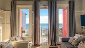 A living room with a view of the ocean, a balcony, and a large window with curtains. - FantaSea On 30A - Gulf View / Pickleball / Deeded Beach Access (Santa Rosa Beach)