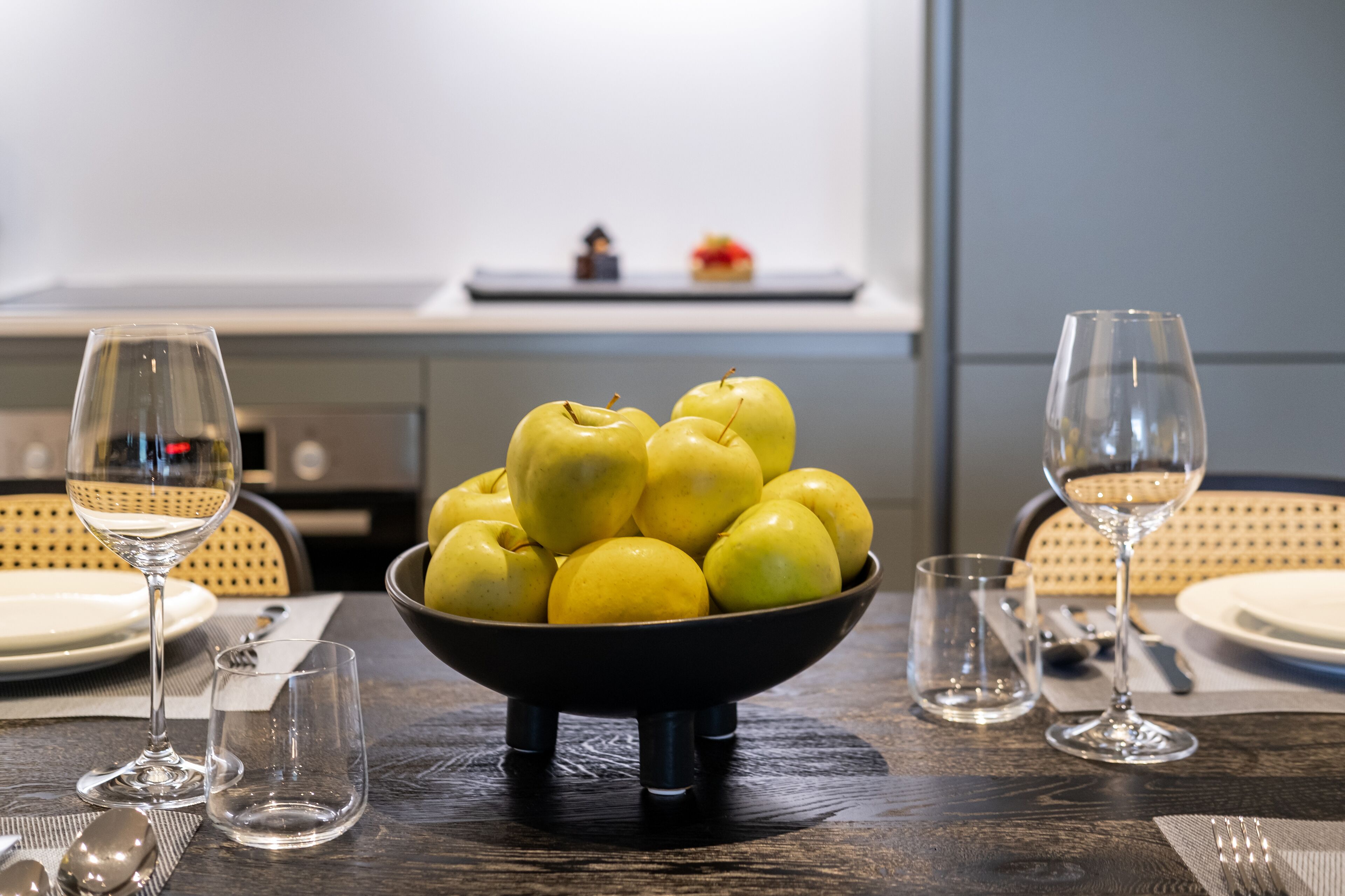 A dining table with a bowl of yellow apples, empty wine glasses, and cutlery.
