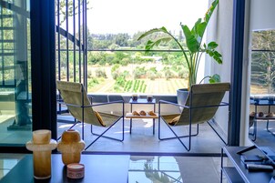 Una habitación moderna con una mesa de vidrio, dos sillas, una mesita con pasteles y una planta grande.