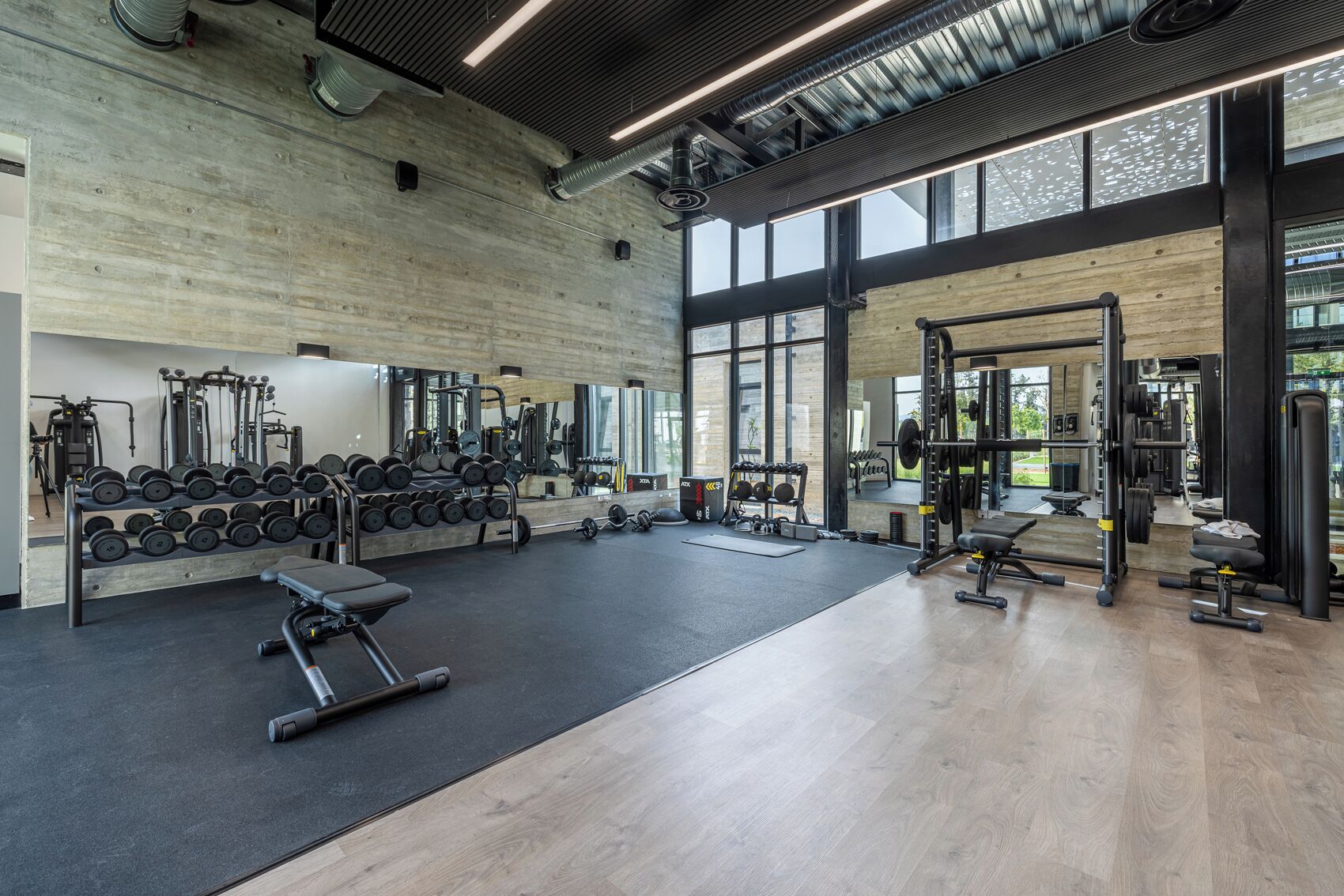 Uma academia ampla com diversos equipamentos de musculação, um banco e um espelho grande na parede.