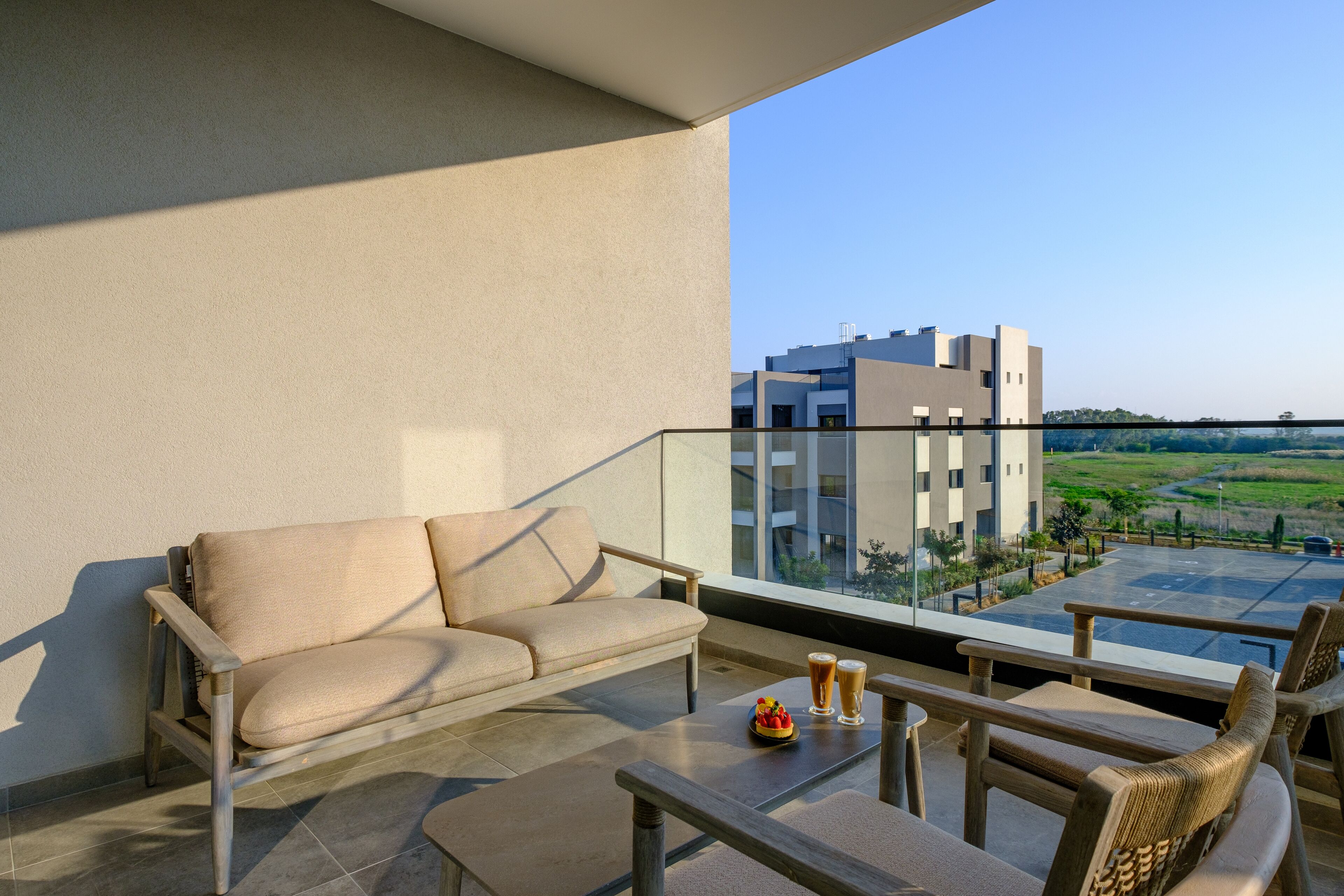 A balcony with a sofa, a table, and two chairs. There are two glasses of beer and a bowl of fruit on the table.