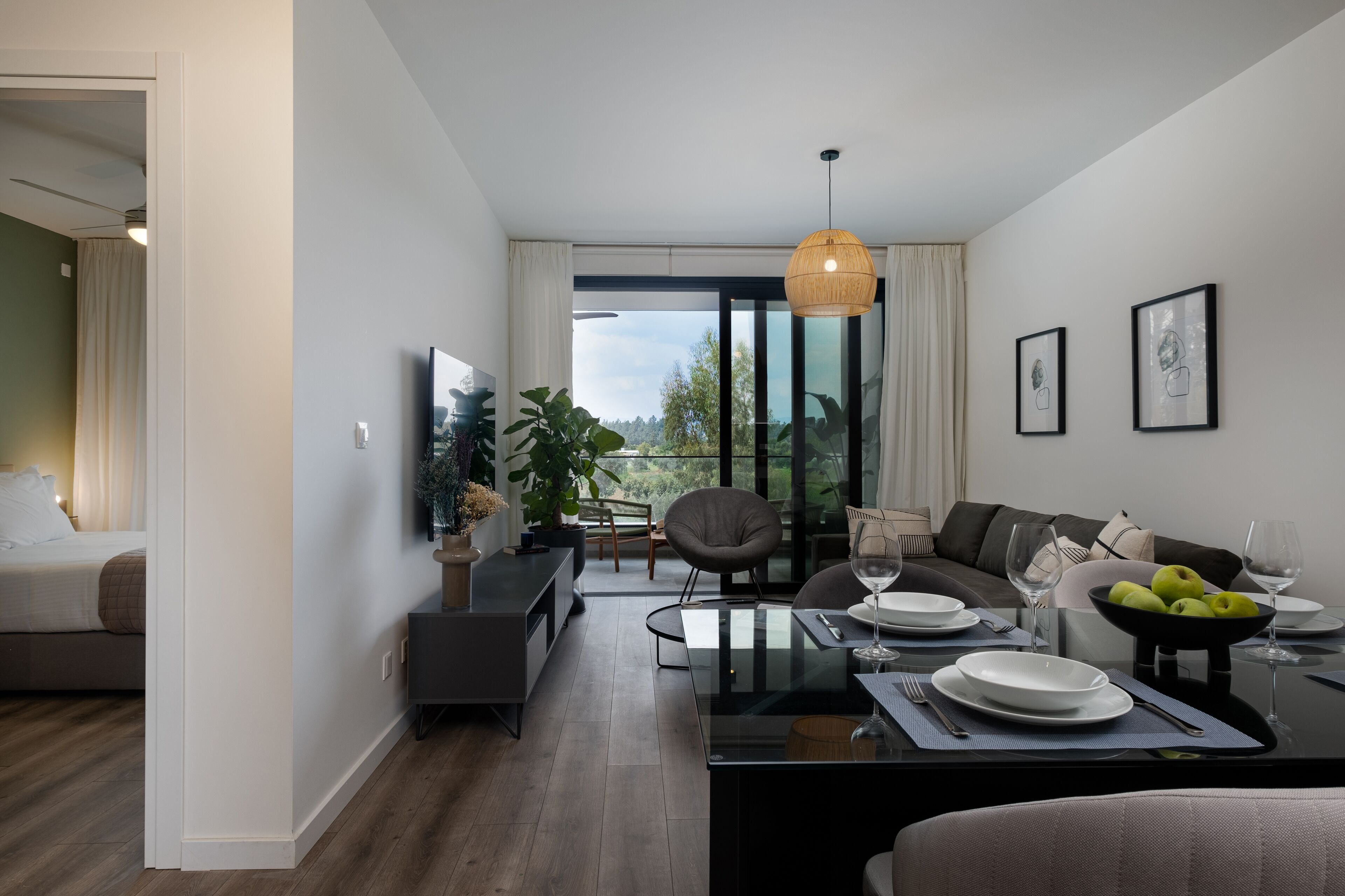 A modern living room with a dining area, large windows, and a view of greenery.