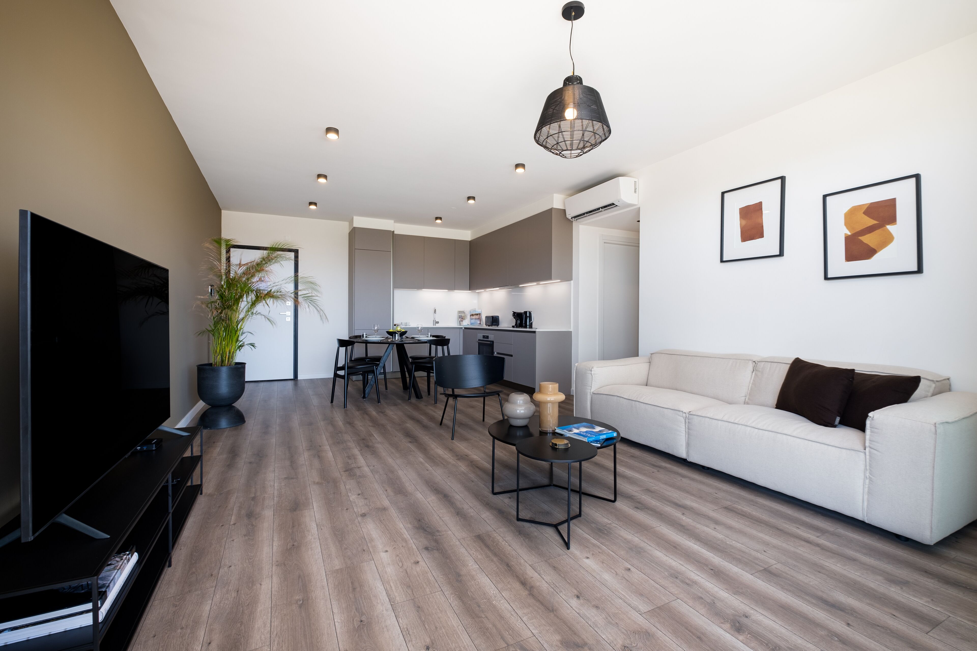 A modern living room with a flat-screen TV, a sofa, a coffee table, and a dining area with chairs and a table.