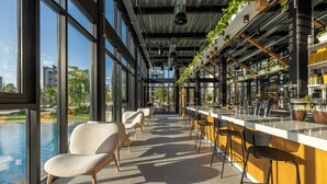 A modern bar area with a long counter, bar stools, and a view of a pool through large windows. - Sunset Gardens (Tserkezoi)