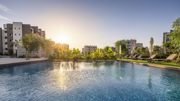 A swimming pool with tiled flooring, surrounded by greenery and modern buildings. - Sunset Gardens (Tserkezoi)