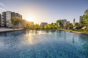 Una piscina con suelo de baldosas, rodeada de vegetación y edificios modernos.