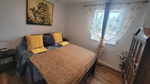 A bedroom with a bed, a nightstand, a window with curtains, a painting on the wall, and a cabinet. - Bright 1 bedroom apartment close to highway, wifi, netflix, prime, free parking (Edmundston)