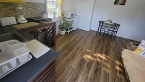 A compact kitchen with a toaster, kettle, and a microwave. There's a dining area with a table and chairs. - Bright 1 bedroom apartment close to highway, wifi, netflix, prime, free parking (Edmundston)
