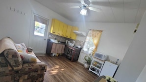 A compact living space with a sofa, a dining table with chairs, a kitchenette, and a ceiling fan. - Bright 1 bedroom apartment close to highway, wifi, netflix, prime, free parking (Edmundston)