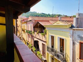 Una hilera de edificios coloridos con balcones, tejados de tejas rojas y vistas a colinas verdes al fondo.