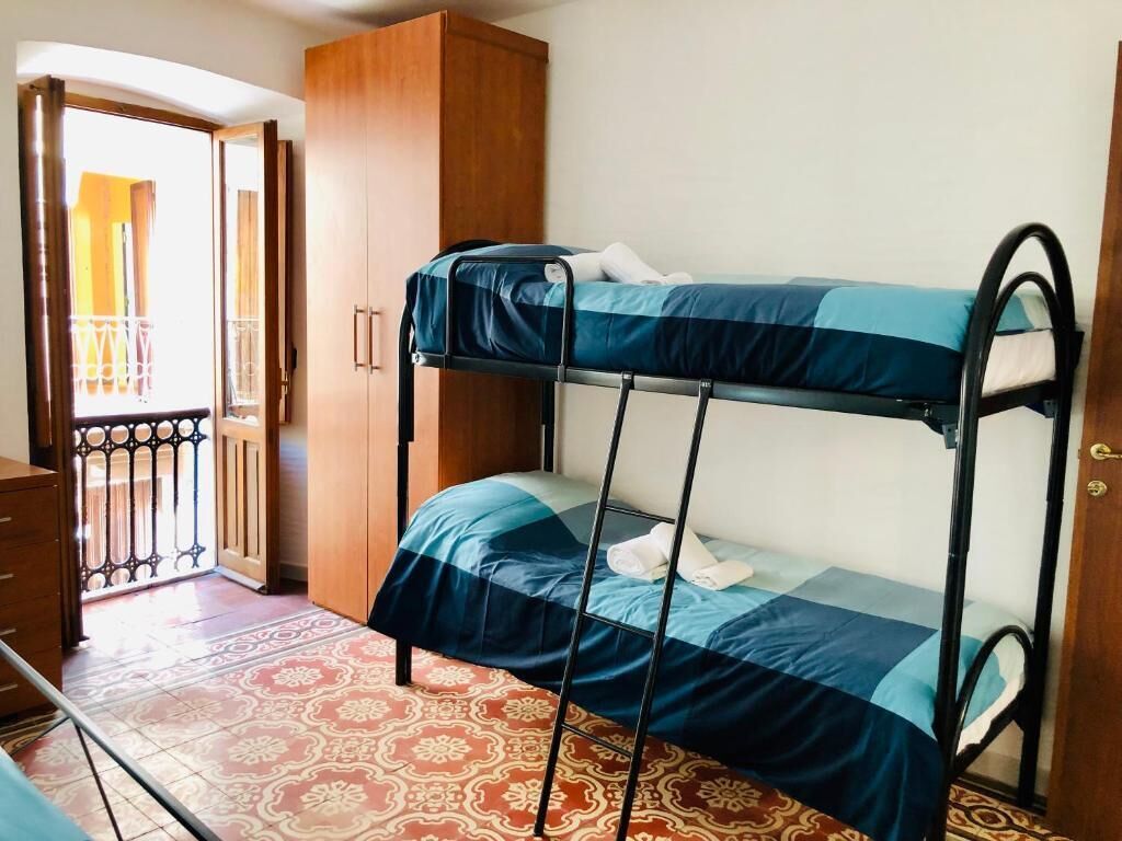 Una cama individual superpuesta con colcha azul y blanca, un armario de madera y suelo estampado.